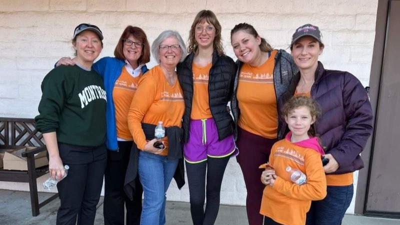A group of women and a young girl wearing orange Run to Feed the Hungry shirts smiling for the camera.