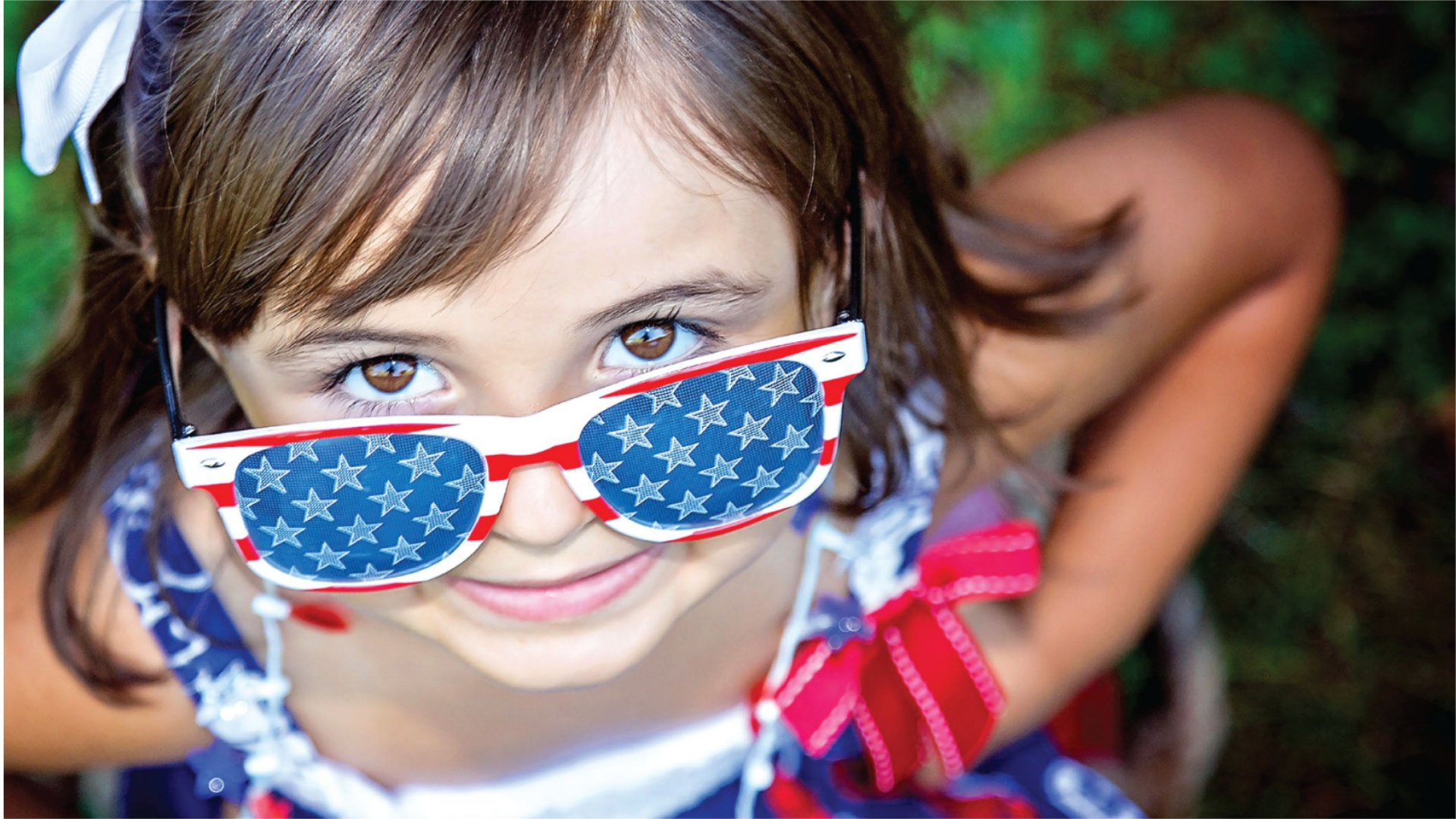 A young girl looking at the camera from above her stars and stripes sunglasses