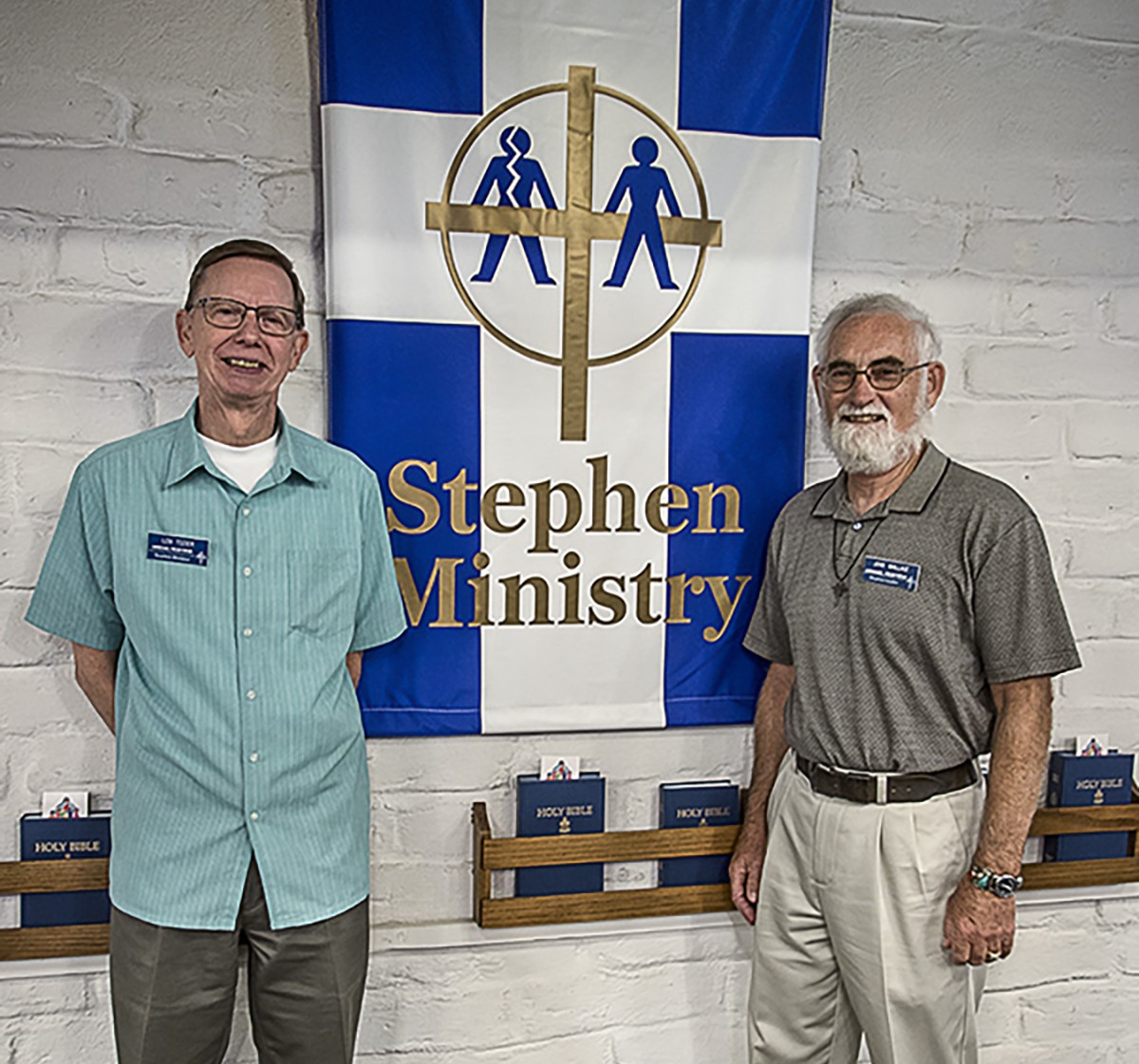Two smiling men standing on either side of a blue and white banner with the Stephen Ministry logo